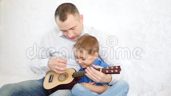 父亲抱着他的小儿子教他弹吉他开朗的孩子拍拍吉他就像她弹吉他一样视频的预览图