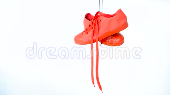 白色背景上挂着一双红色女运动鞋鲜艳的珊瑚女人的训练器挂在绳子上视频的预览图
