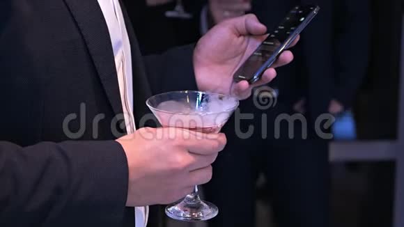一个穿着经典西装的体面男人手里拿着一杯吸烟鸡尾酒在聚会上用手机创意创意视频的预览图