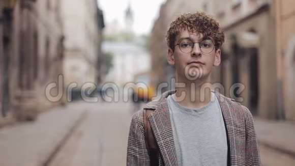 年轻的嬉皮士背包站在城市街道上看镜头的肖像旅游旅游视频的预览图