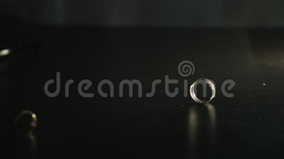 婚礼戒指在黑色镜面上闪耀着光并滚动在一起视频的预览图