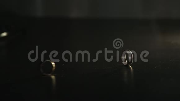 婚礼戒指在黑色镜面上闪耀着光并滚动在一起视频的预览图