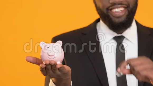 穿西装的黑人微笑着把硬币放在储蓄罐里资本投资储蓄视频的预览图
