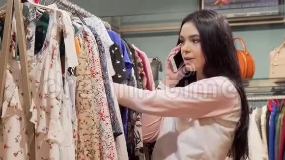 迷人的年轻女人在买衣服的时候打电话视频的预览图