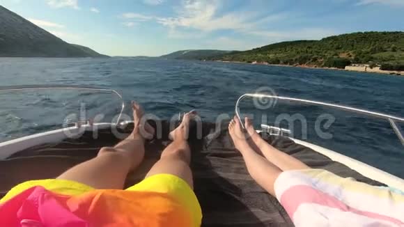 男子和妇女的双腿躺在游艇上驾驶着蓝绿色的大海和海滩上面有绿棕榈树视频的预览图