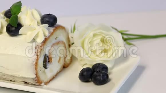 海绵蛋糕涂上奶油用干蓝莓和新鲜薄荷叶装饰附近躺着一朵白玫瑰特写镜头视频的预览图