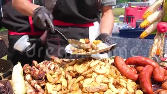 街头美食节一位穿着黑色衣服和手套的厨师把油炸食品铺在盘子上土豆烤香肠肉视频的预览图