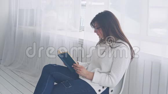 一个戴眼镜的年轻女孩坐在椅子上看书视频的预览图