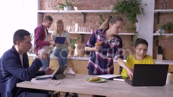 成功的年轻商人们正在厨房里用平板电脑和笔记本电脑吃饭和工作视频的预览图