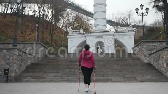 年轻的胖乎乎的有魅力的女性走上楼梯用电线杆行走北欧减肥概念视频的预览图