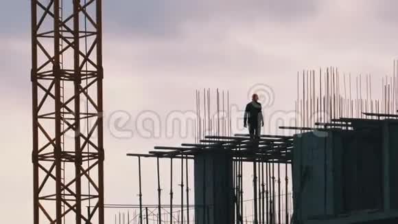 正在建造的摩天大楼边缘上的建筑者的剪影施工现场的工人视频的预览图