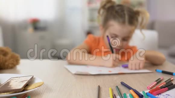 女儿吃着妈妈亲手做的甜点在桌上用铅笔画画视频的预览图
