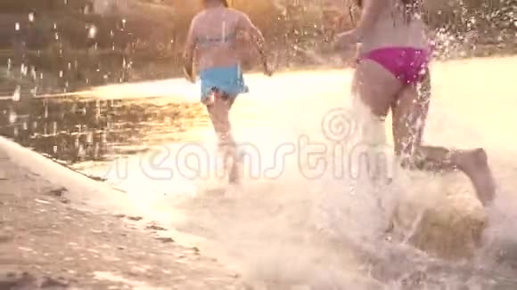 快乐的孩子们沿着海滩奔跑女孩们在沙滩上奔跑在海滩上溅起水滴笑着快乐和快乐视频的预览图
