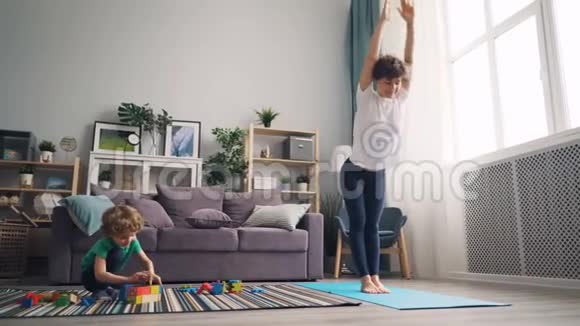 灵活的女人在家里练习瑜伽而她的小儿子在玩积木视频的预览图