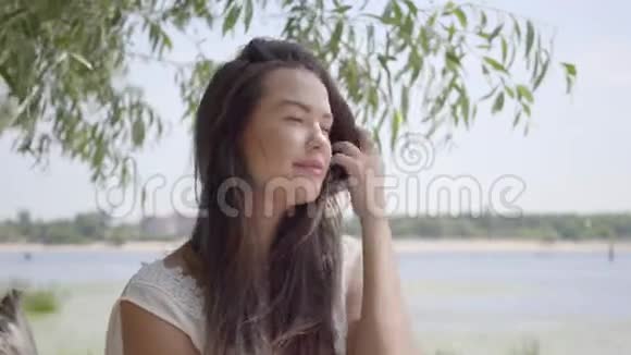 一位美丽迷人的少女一头深色长发穿着白色的夏装坐在海滨视频的预览图