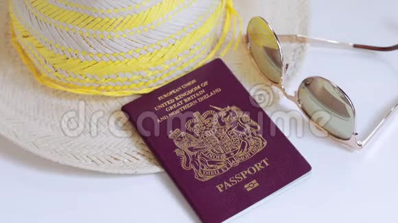 一只手从白色的桌子上拿起一本英国护照太阳镜和一顶夏季帽子视频的预览图