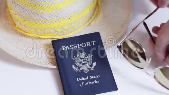 一只手从白色的桌子上拿起一本美国护照太阳镜和一顶夏季帽子视频的预览图