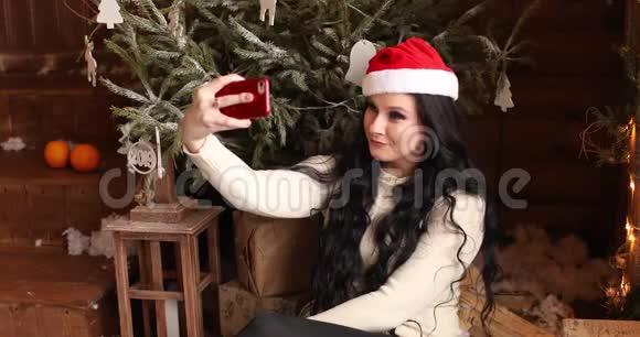 漂亮的女人长发戴着圣诞帽在圣诞树上自拍视频的预览图