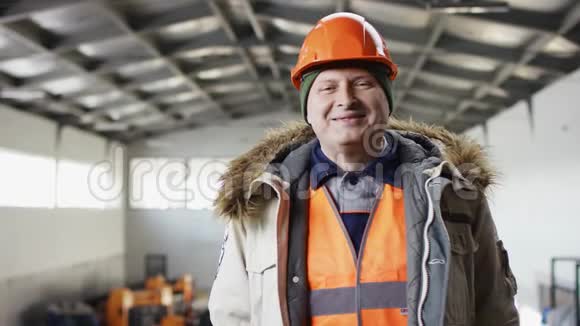 戴着安全帽穿着工作服的人正站在机库中间微笑着看着摄像机视频的预览图