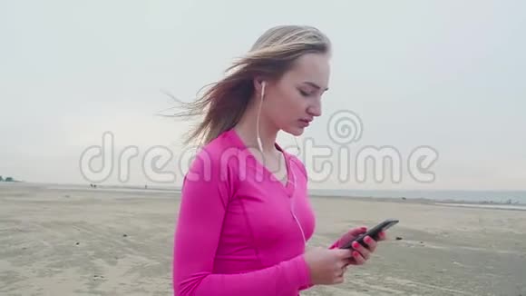 穿着运动衫在沙滩上听音乐的女孩通过耳机视频的预览图