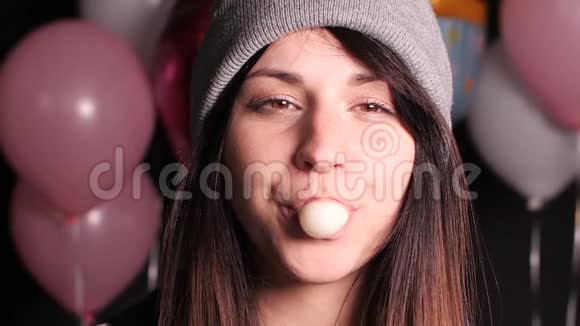 戴着灰色帽子的女孩吹着粉红色的大泡泡直到它破裂视频的预览图