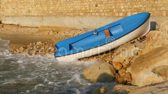孤独的白蓝色小船靠在岩石海岸的砖墙上海浪拍打着海岸景色优美视频的预览图