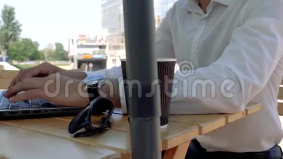 一个穿着白色衬衫坐在街边咖啡馆里用手提电脑键盘打字的男人的双手紧闭商人打字视频的预览图