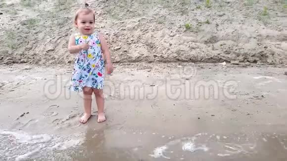 一个小女孩穿着一件花裙子站在河岸上的洞穴里很高兴视频的预览图