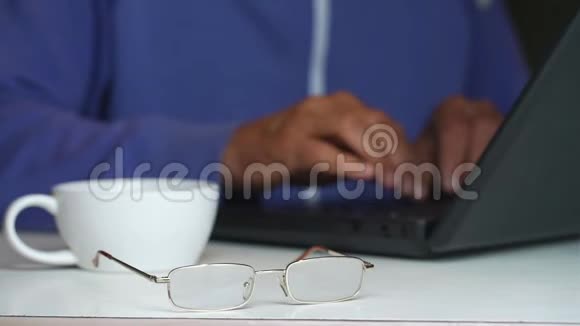 杯子和眼镜躺在老人手提电脑特写上打字视频的预览图