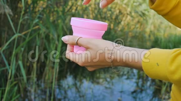 女性双手打开一个装有粉红色硅胶月经杯的容器展示出来放在绿色自然背景上视频的预览图