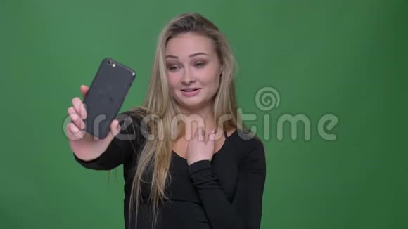 年轻女商人穿着黑色衬衫在绿色背景下的智能手机上愉快地在视频聊天视频的预览图