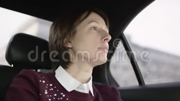 穿着白色衬衫和栗色毛衣的棕色头发的漂亮女人坐在车里解释去她家的正确方式视频的预览图