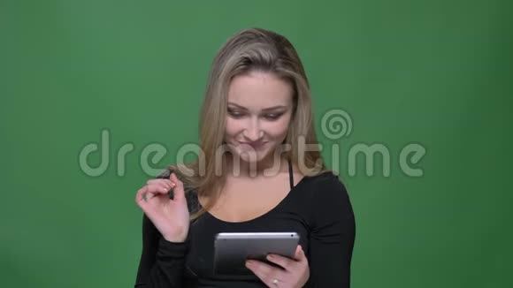 穿着黑色衬衫的女商人在绿色背景下微笑着看着平板电脑视频的预览图
