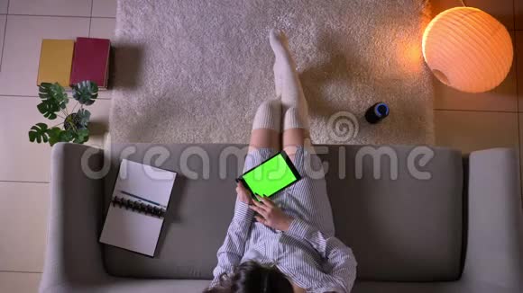 年轻迷人的女性在平板电脑上的特写镜头绿色的彩色屏幕坐在沙发上视频的预览图