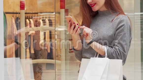 女人微笑着一边在商场购物一边浏览她的智能手机视频的预览图