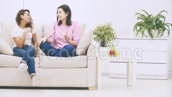 可爱的白种人和非洲裔美国女孩坐在沙发上交谈友好和情感微笑视频的预览图