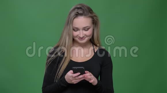 年轻女商人穿着黑色衬衫在绿色背景下微笑着看着智能手机的肖像视频的预览图