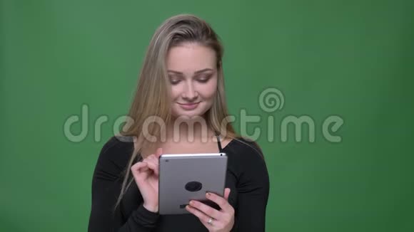 快乐的女商人穿着黑色衬衫展示蓝色平板电脑屏幕在绿色背景下推荐应用程序视频的预览图