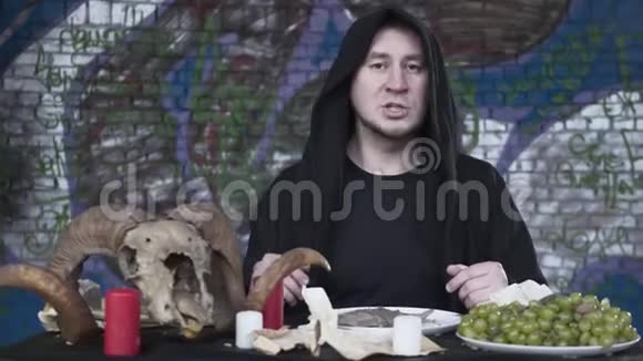 一个穿着黑色衣服头上戴着头巾的可疑男人坐在蜡烛前的小桌子旁葡萄视频的预览图