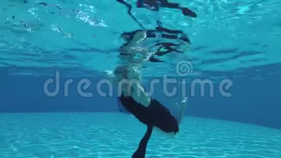 一个迷人的年轻金发女郎穿着一件黑色的衣服在水下游泳手臂伸出水面视频的预览图