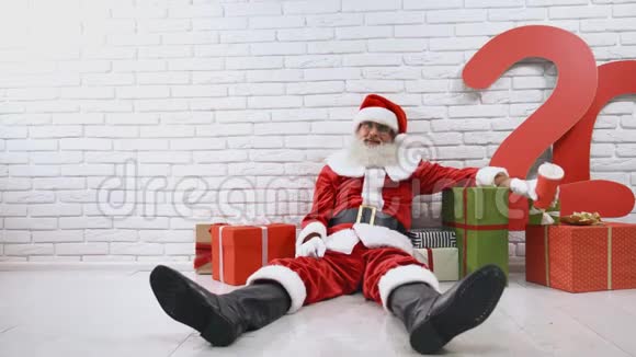 穿着圣诞老人服装的老人坐在有礼品盒的工作室里视频的预览图