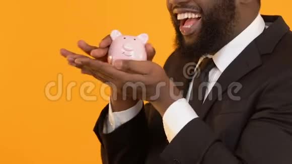 兴奋的黑色男性西装革履地摇着储蓄罐等待创业利润视频的预览图