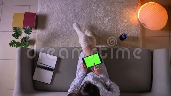 一位年轻迷人的女青少年在沙发上用绿色的彩色屏幕发送平板电脑的特写镜头视频的预览图