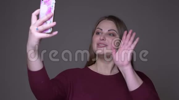 一位年轻的超重白种人女性的特写镜头她在电话上打了个视频电话背景是灰色的视频的预览图