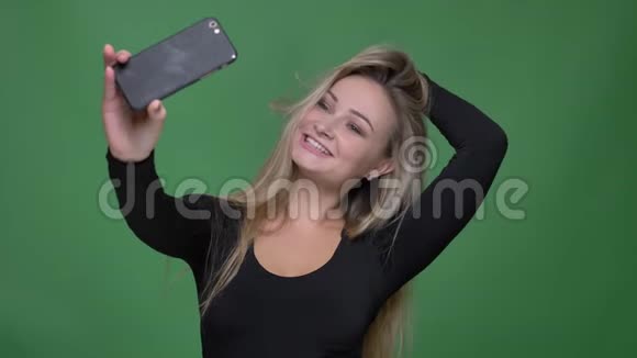 年轻模特的肖像黑色衬衫固定头发并制作自拍照片使用智能手机在绿色背景视频的预览图