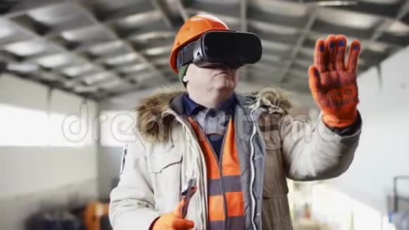 戴着安全帽穿着工作服的人正站在机库中间在虚拟现实中用扳手工作视频的预览图
