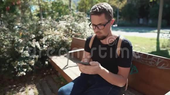 独自一个男性游客在他的智能手机屏幕上观看坐在公园里视频的预览图