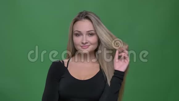 年轻女商人穿着黑色上衣在绿色背景下用相机和旋转的头发绕着手指调情的肖像视频的预览图