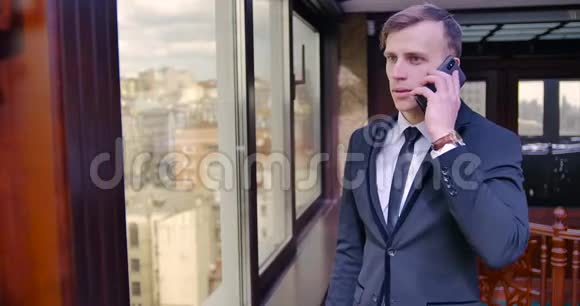 一个穿西装的年轻人站在办公室的窗户附近打电话挂断电话高兴起来满意视频的预览图