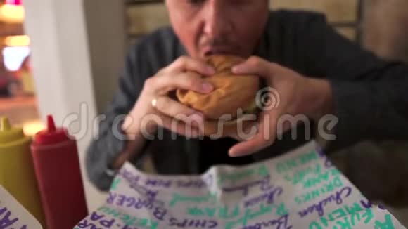 成人在咖啡馆里咬着多汁的汉堡包近距离观看视频的预览图